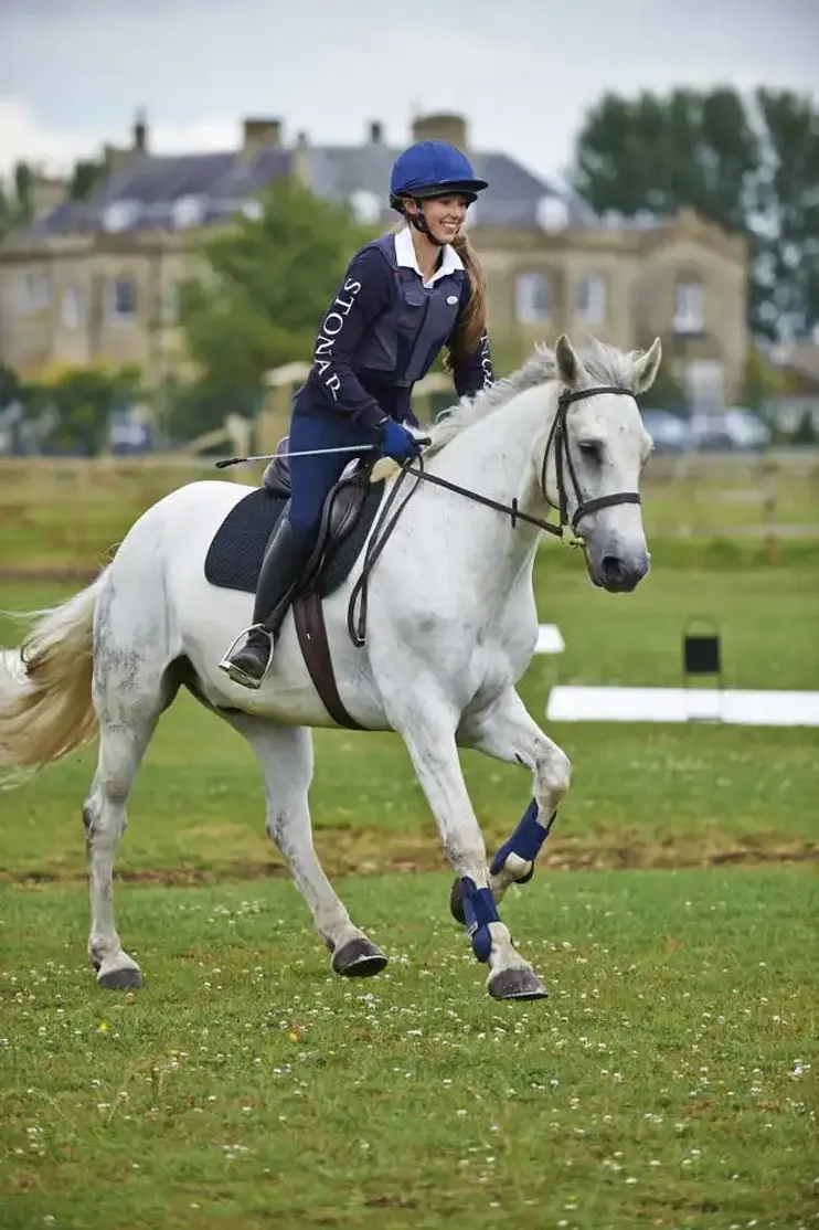 Studentessa in tenuta da equitazione monta un cavallo bianco durante un'attività a scuola