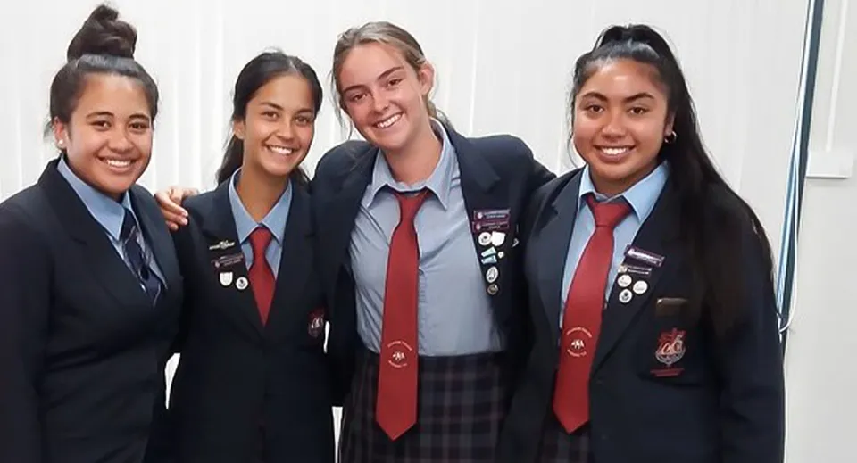 Quattro studentesse in uniforme scolastica mettono in posa insieme all'interno di un'aula nel campus del Cullinane College.