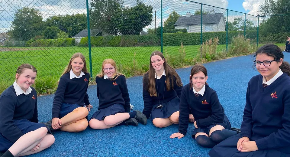 Studentesse della Meán-Scoil Mhuire Gan Smál in uniforme siedono su una superficie in gomma blu nell'area esterna della scuola.