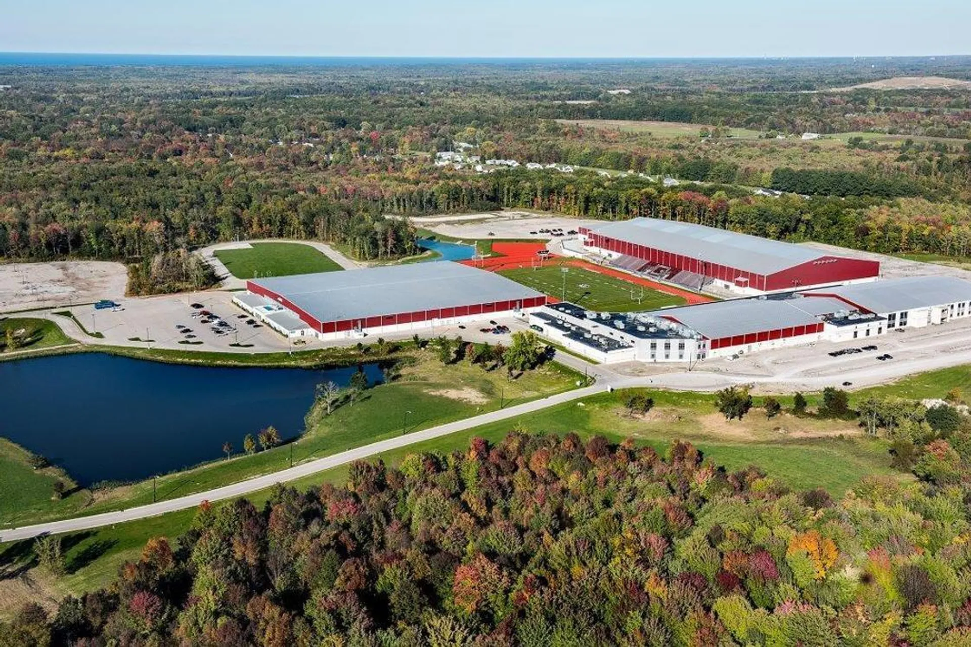 Il complesso agricolo della SPIRE Academy con tetti rossi si trova immerso in un paesaggio boschivo vicino a uno stagno.