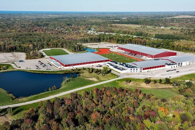 Il complesso agricolo della SPIRE Academy con tetti rossi si trova immerso in un paesaggio boschivo vicino a uno stagno.