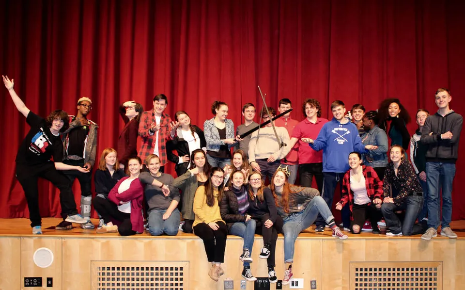Un gruppo di studenti e studentesse della Milton District High School si trova insieme su un palco davanti a un sipario rosso.