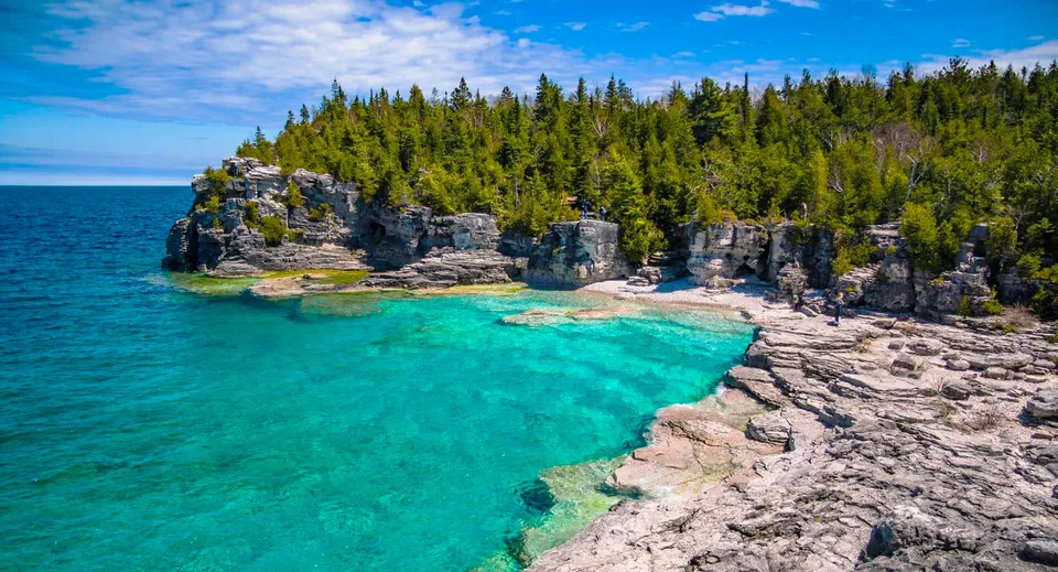 Una costa rocciosa con acque turchesi trasparenti e una foresta verde sulla scogliera.