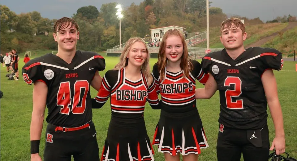 Quattro studenti e studentesse in divise sportive nere e rosse della Bishop Rosecrans High School sono insieme su un campo sportivo.