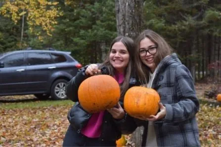 Dos estudiantes sostienen sonrientes sendas calabazas de Halloween en un bosque otoñal