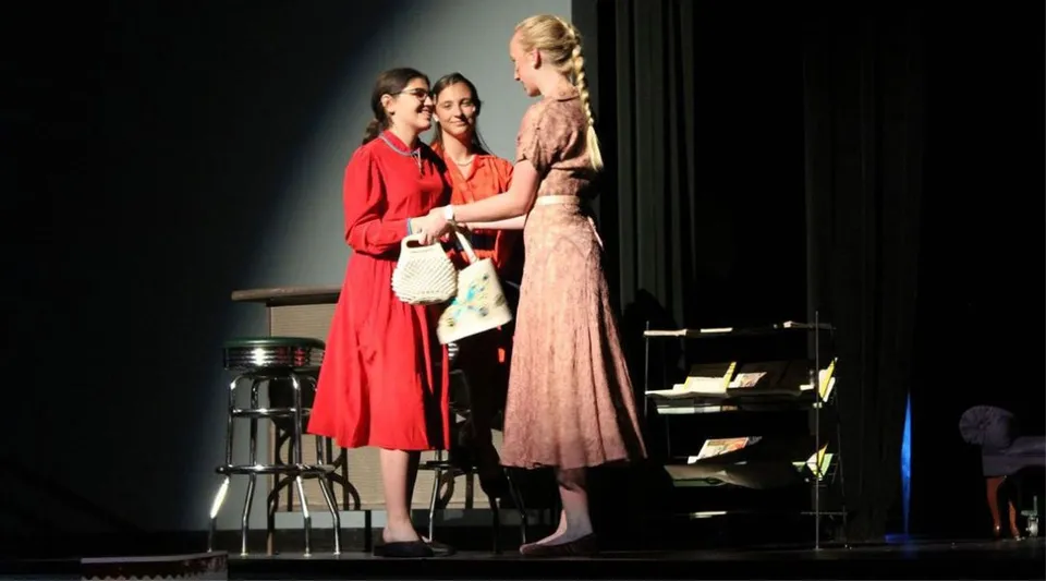 Tre studentesse della University Lake School in abiti di scena si trovano sul palco di un teatro.