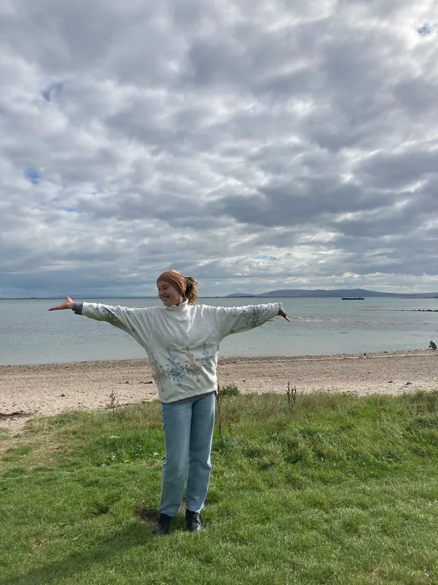 Chica con los brazos abiertos sobre la hierba junto a una playa y el mar
