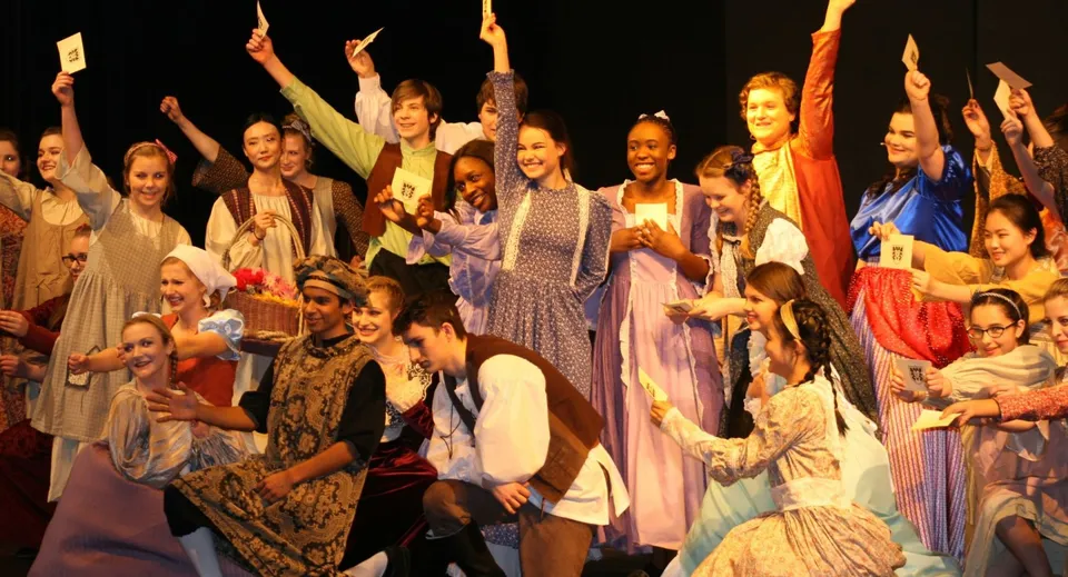 Un gruppo di studentesse della Rothesay Netherwood School festeggia in costumi colorati con le braccia alzate.