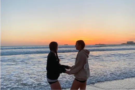Zwei Mädchen halten bei Sonnenuntergang am Strand in Spanien Händchen