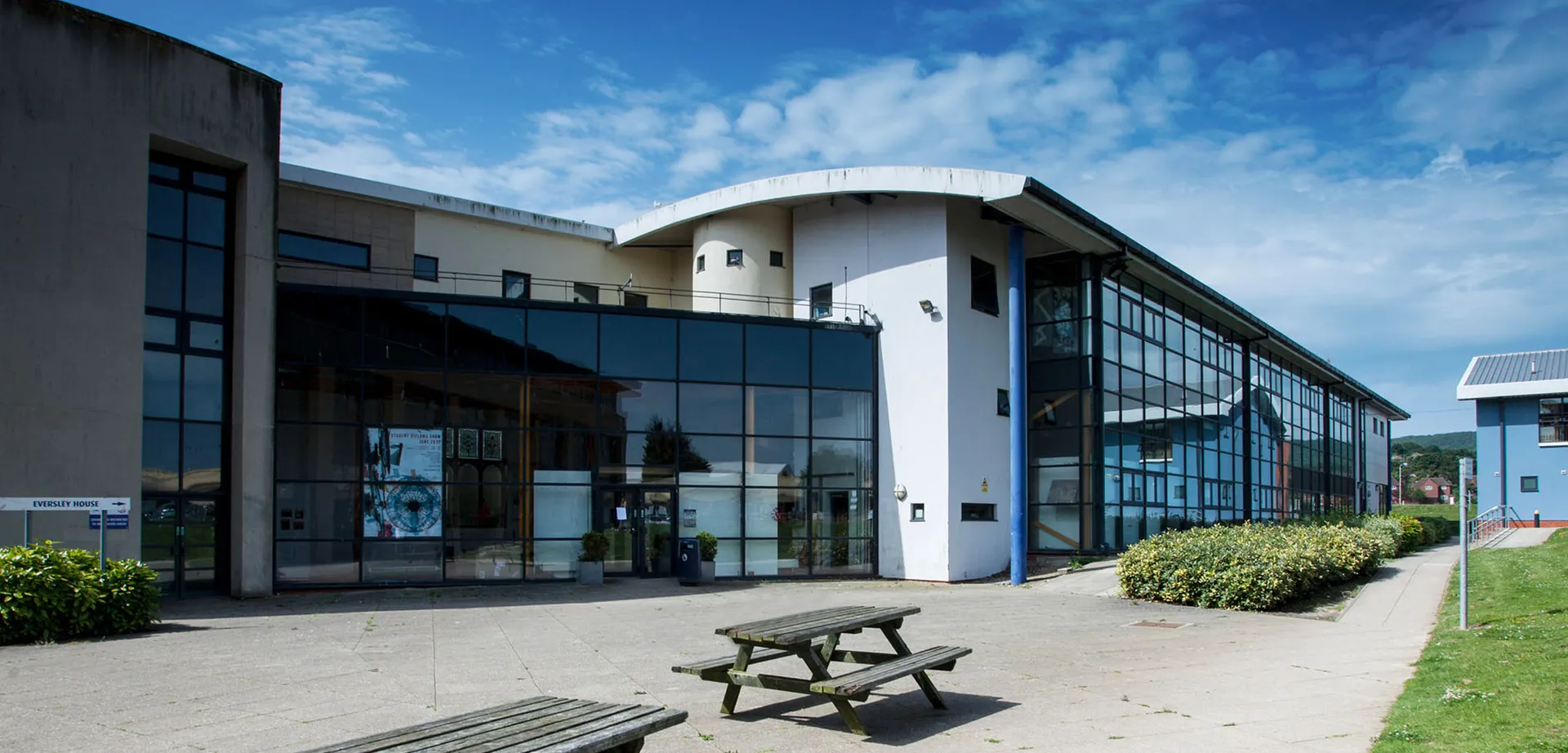 L'edificio moderno del East Sussex College Eastbourne con ampie vetrate e tavoli da picnic nel cortile.