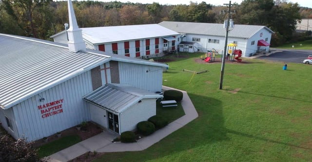 Das Gebäude der Harmony Christian School steht neben einem Spielplatz und einem grünen Bereich mit Wald im Hintergrund.