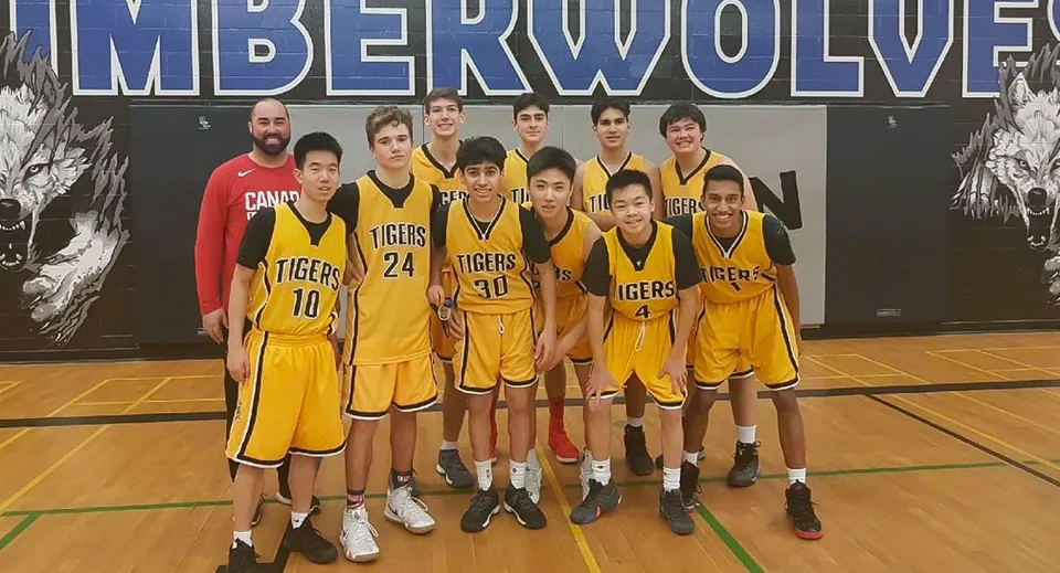 Un gruppo di giovani giocatori e giocatrici di basket della Thornhill Secondary School posa davanti a uno striscione dei Timberwolves sul campo da basket.