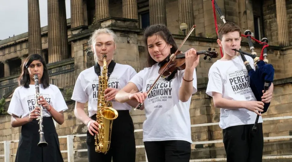 Un gruppo di giovani musicisti suona diversi strumenti davanti all'edificio classico della St. Mary’s Music School.