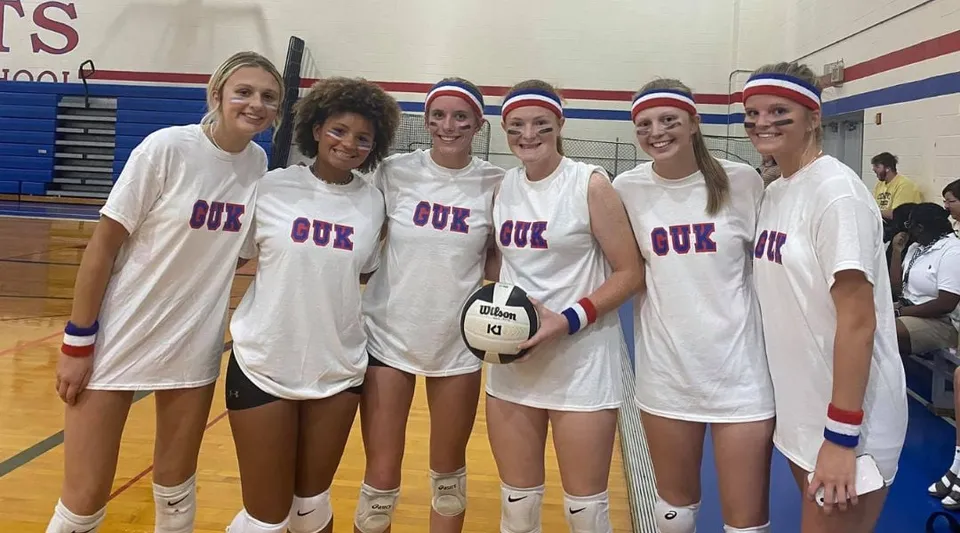 Un gruppo di studentesse della Kokomo Center Township Consolidated School Corporation è insieme in palestra, con uniformi sportive bianche.
