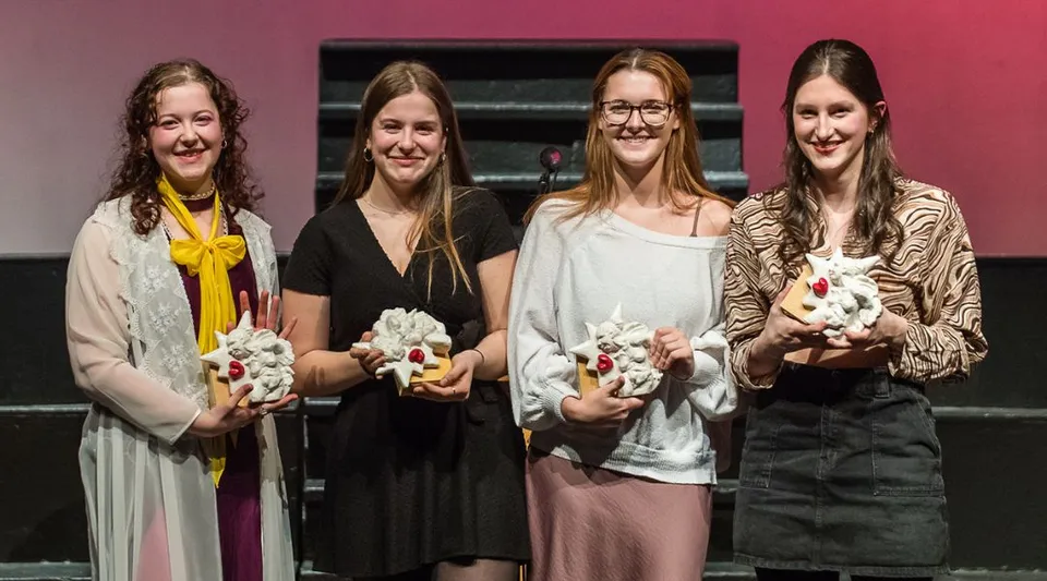 Quattro studentesse della Massey-Vanier High School stanno in piedi con mazzi di fiori bianchi davanti a uno sfondo rosa e nero.