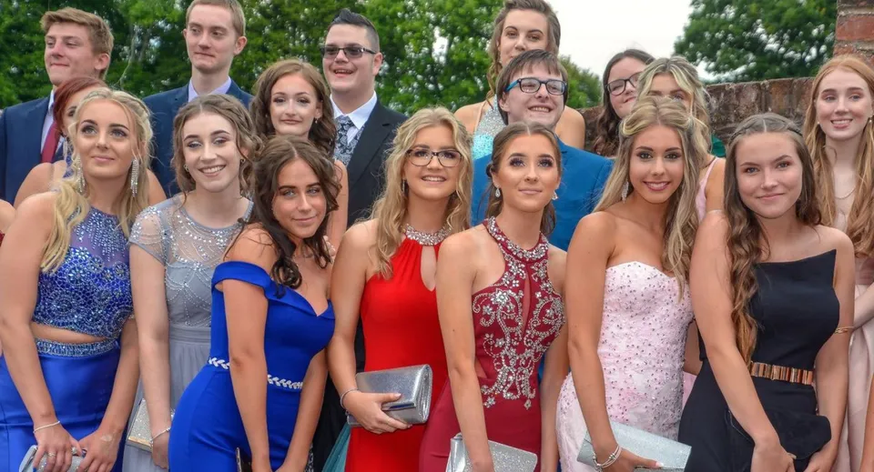 Un gruppo di giovani in abito formale posa all'aperto davanti agli alberi nel terreno della Sidcot School.