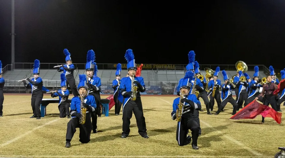 Un gruppo di studenti del Chandler Unified School District in divisa blu e nera si trova su un campo davanti a una struttura simile a uno stadio.