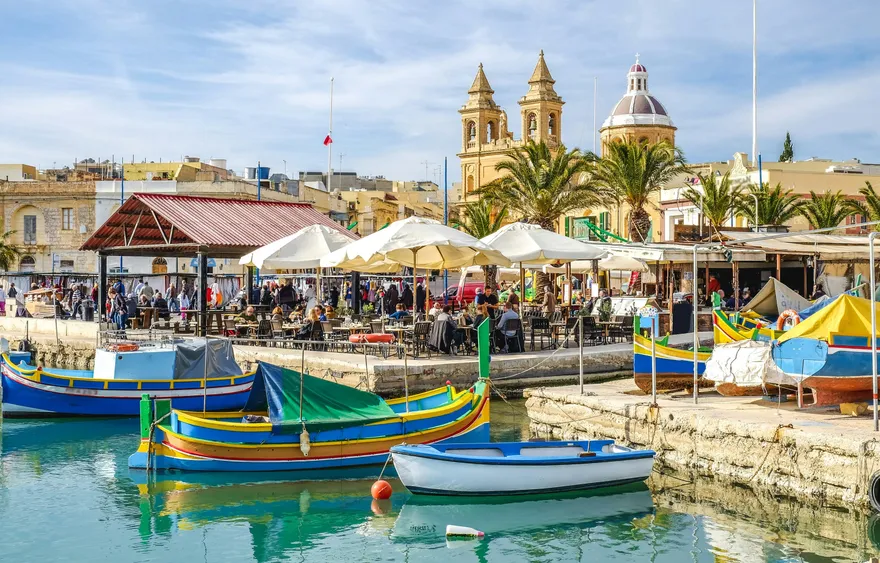 Puerto de Malta con barcas de colores en el agua y la iglesia del pueblo al fondo