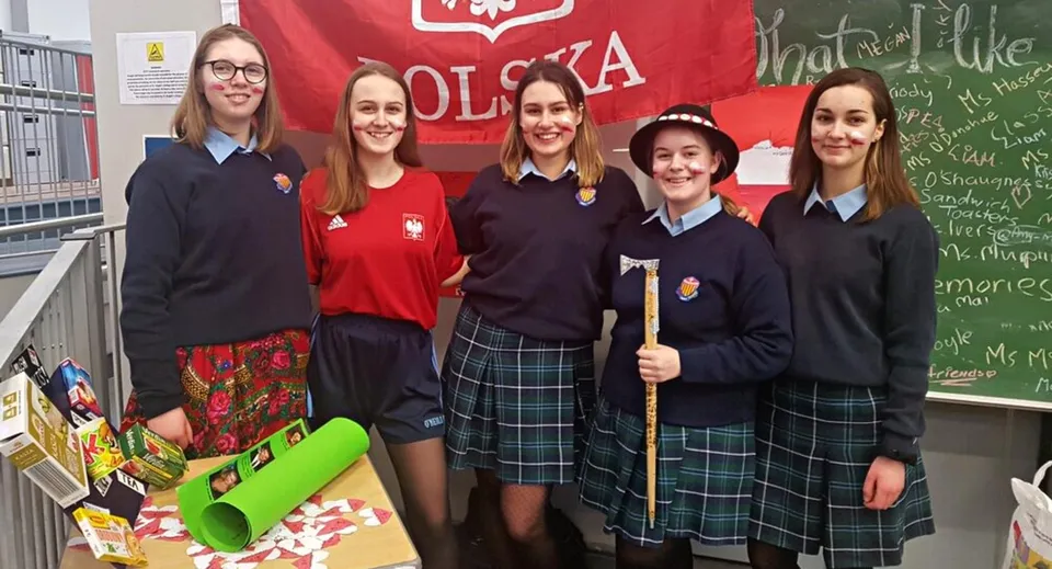 Un gruppo di studentesse del St. Brigid's College si trova davanti a una bandiera bianca e rossa con l'emblema dell'aquila polacca.