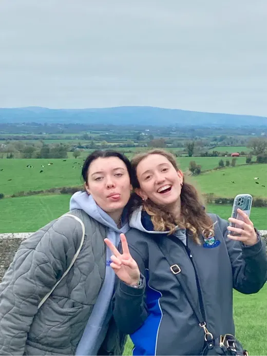 Zwei Mädchen machen ein Selfie vor den grünen Wiesen der Landschaft in Irland