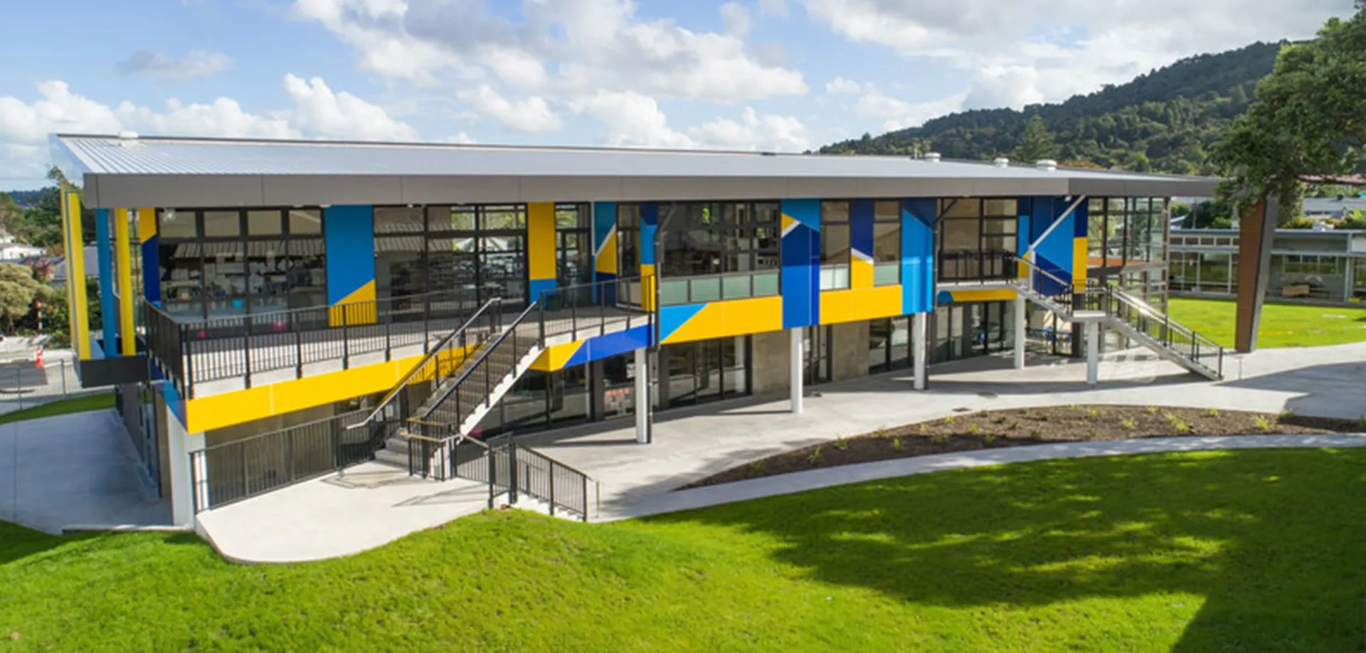 L'edificio moderno e colorato della Whangarei Girls High School con grandi finestre e un prato in primo piano davanti a colline boscose.