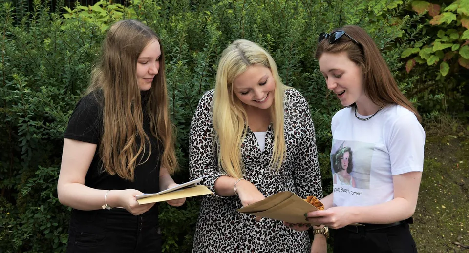 Tres estudiantes de la St. Edward's School en Poole miran juntas un libro en el área exterior verde.