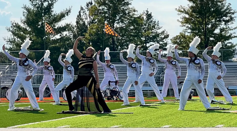 Un gruppo di performer in outfit bianco e nero si trova su un prato all'interno della Mater Dei Catholic High School.