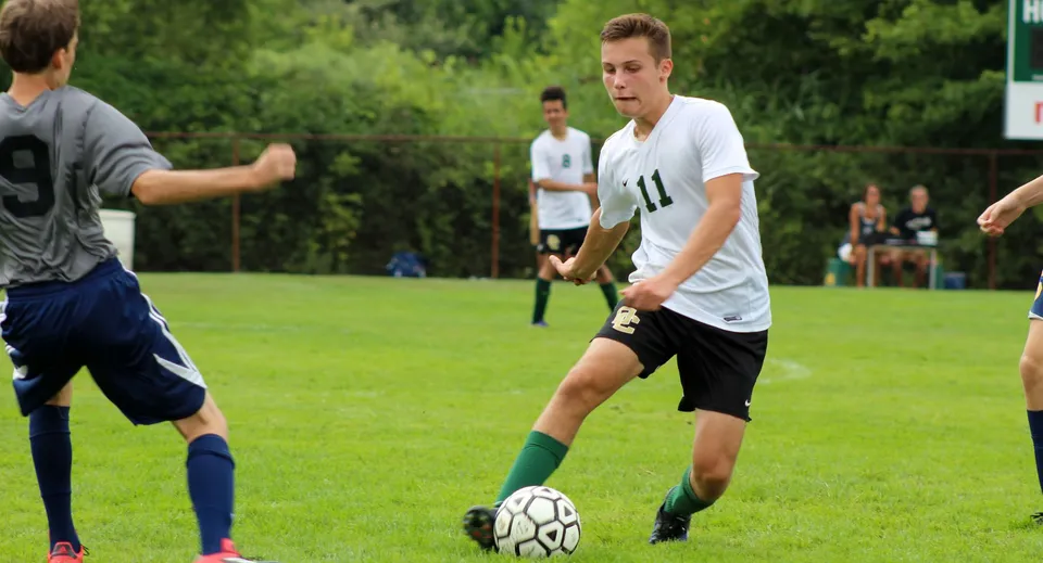 Due studenti giocano a calcio sul campo in erba della Oakland Christian School con altri giocatori sullo sfondo.