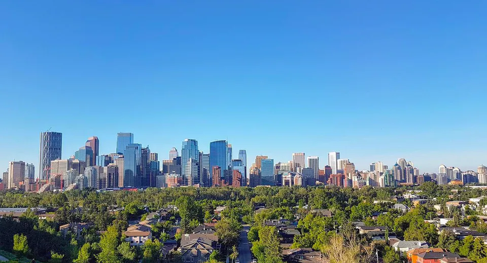 Panorama dello skyline cittadino con moderni grattacieli e alberi verdi sotto un cielo limpido.