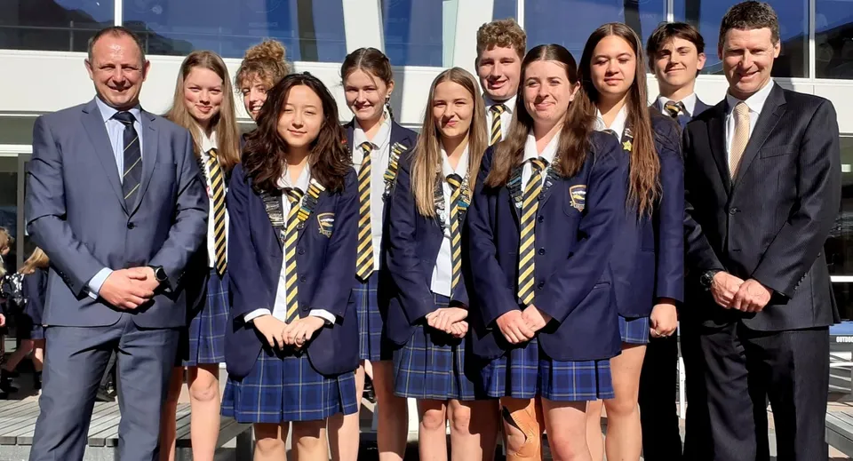 Un gruppo di studenti e studentesse della Wakatipu High School posa davanti a un edificio moderno con grandi finestre.
