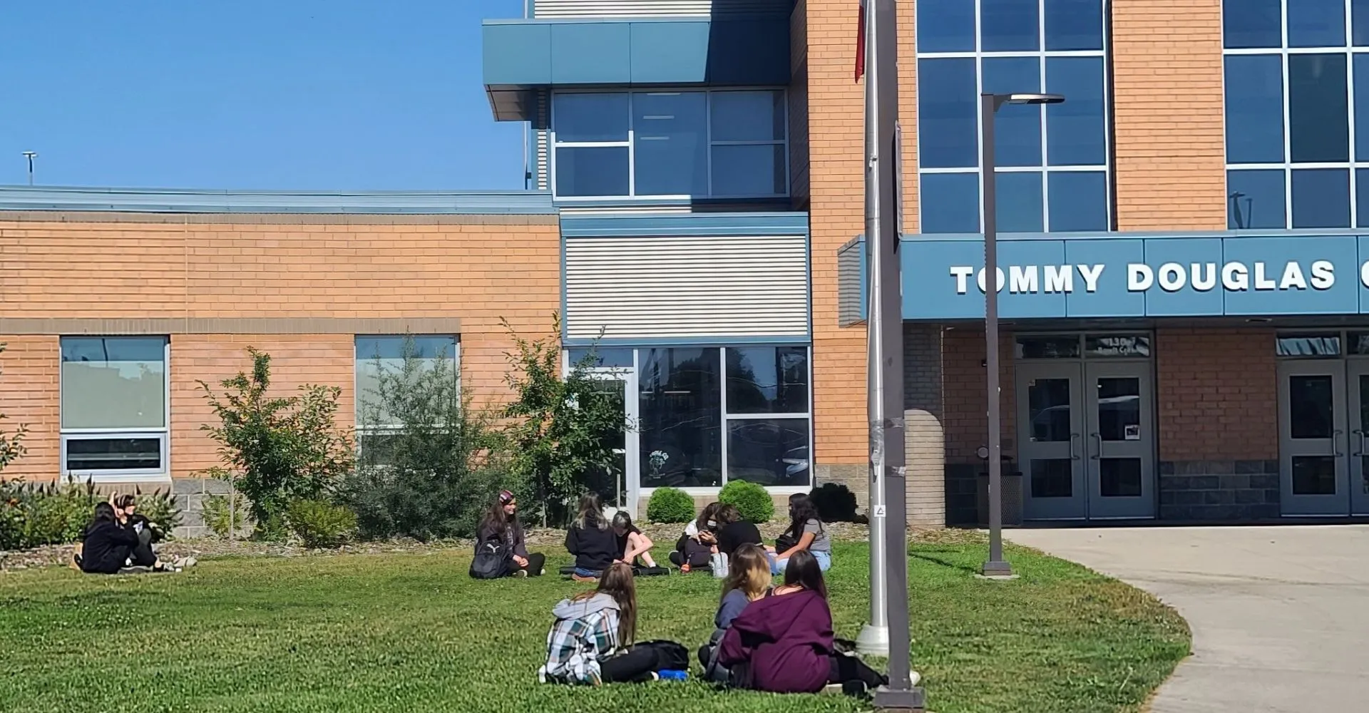 Persone sedute sul prato davanti al moderno edificio del Tommy Douglas Collegiate.