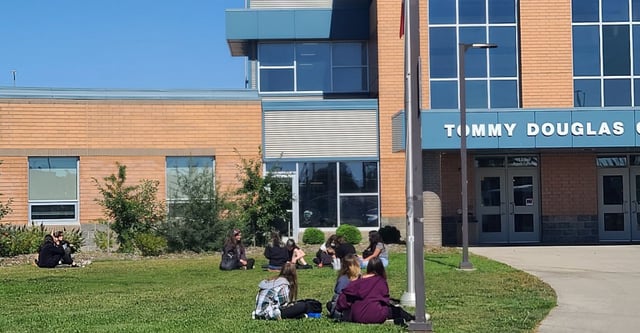 Persone sedute sul prato davanti al moderno edificio del Tommy Douglas Collegiate.