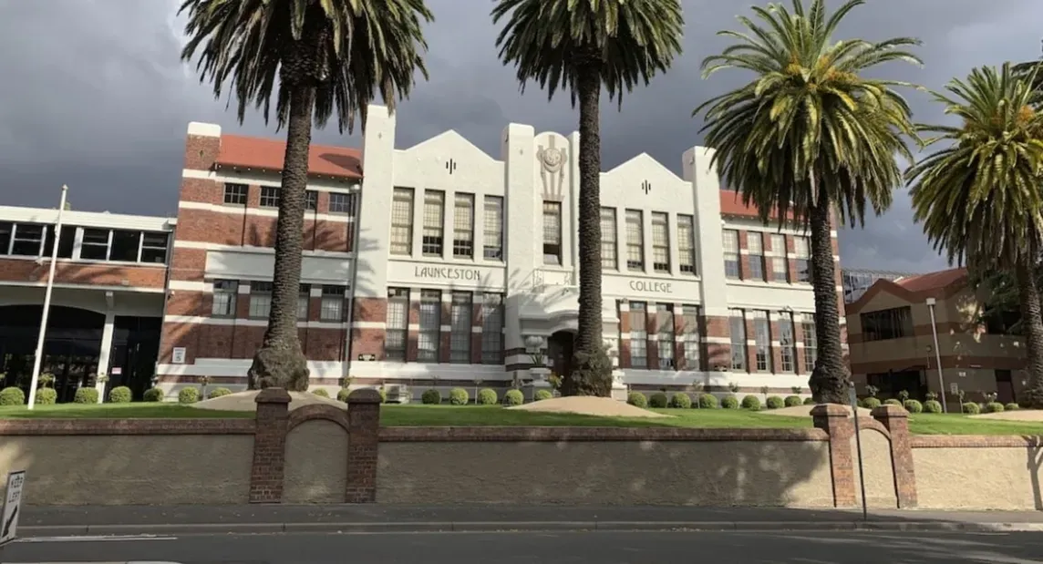 Edificio escolar histórico con fachada art déco y altas palmeras delante, con nubes oscuras al fondo