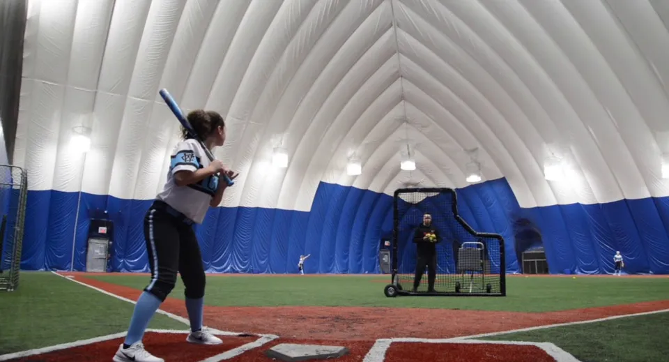 Una studentessa della Northeastern Wisconsin Lutheran High School è in piedi sul campo da baseball davanti a una struttura gonfiabile blu e bianca.