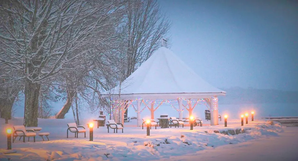 Un gazebo innevato con lanterne illuminate e sedie nel campus della Orillia Secondary School in un paesaggio invernale.