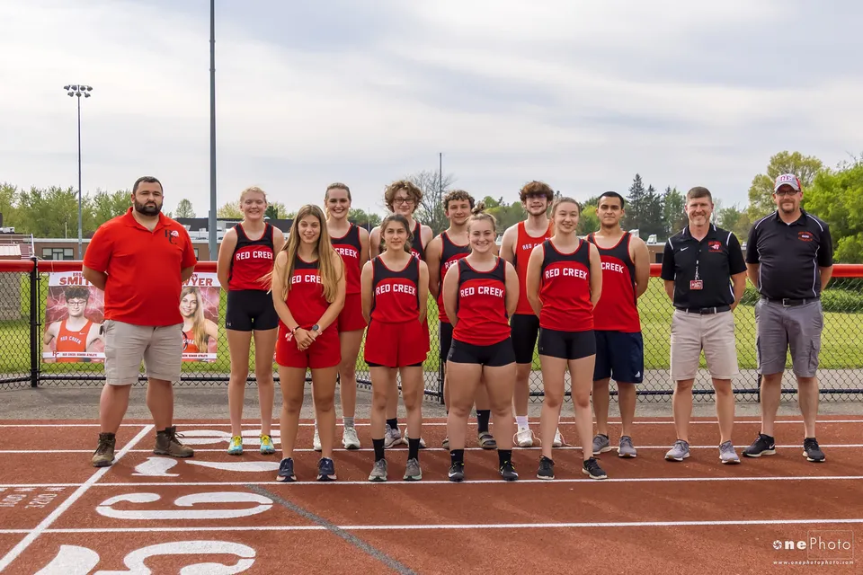 Un gruppo di atleti in uniformi rosse si trova sul campo sportivo della Red Creek High School sotto un cielo nuvoloso.