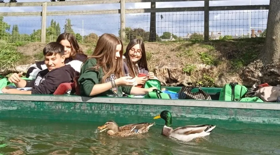 Studenti del Colegio Argantonio sono seduti su una panchina e guardano un laghetto con anatre che nuotano in un ambiente rurale.