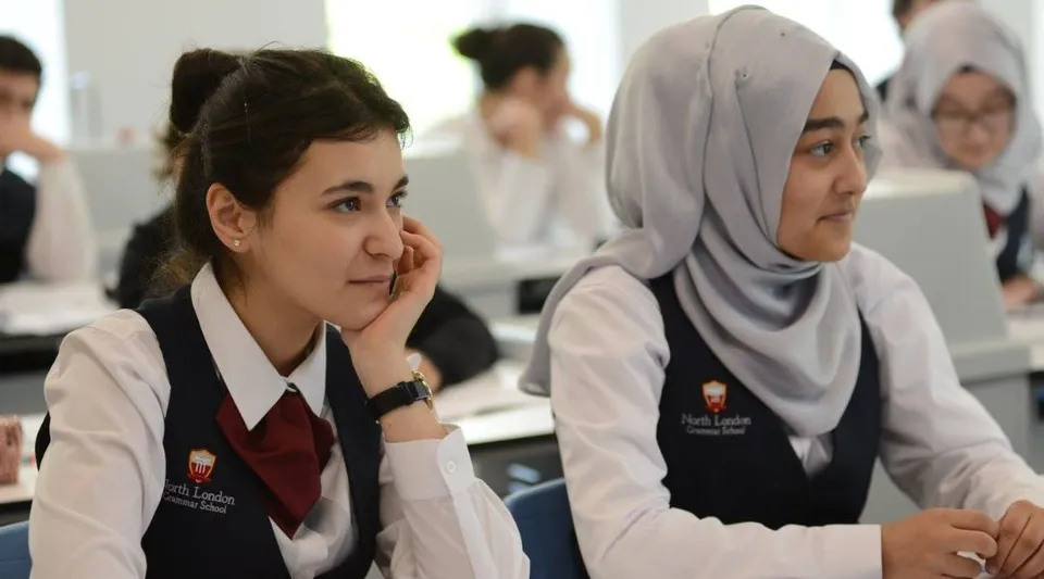 Due studentesse della North London Grammar School in uniforme scolastica sono sedute a un banco in classe.