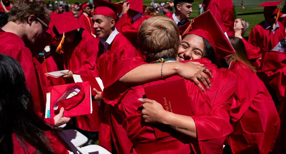 Un gruppo di neodiplomati in toga rossa si abbraccia su un prato del campus delle St. Vrain Valley Schools.