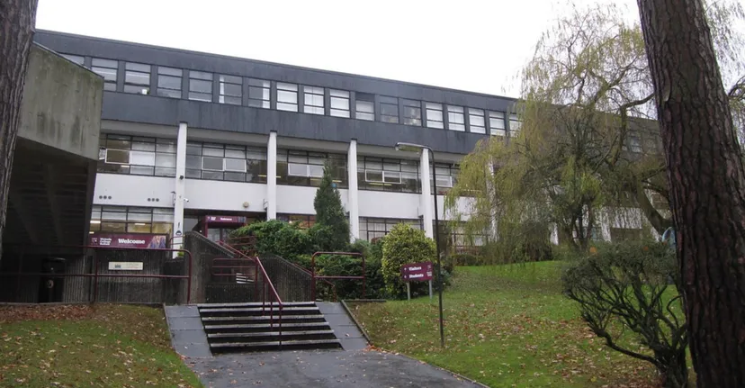 L'edificio grigio a più piani nel campus del Victoria College Belfast è circondato da alberi e verde.