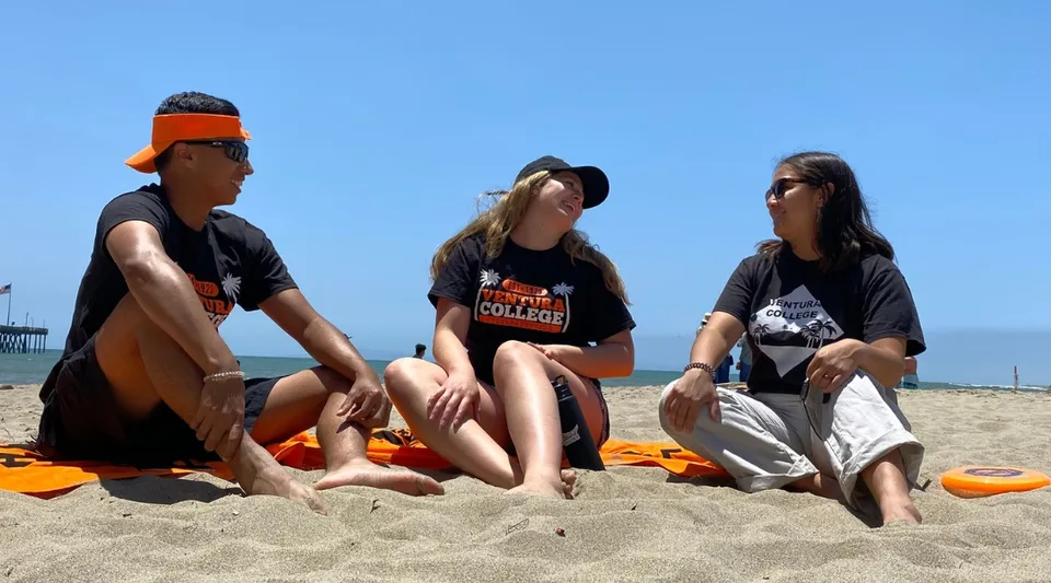 Tre persone sono sedute in spiaggia sotto un cielo azzurro nel campus del Ventura County Community College District.