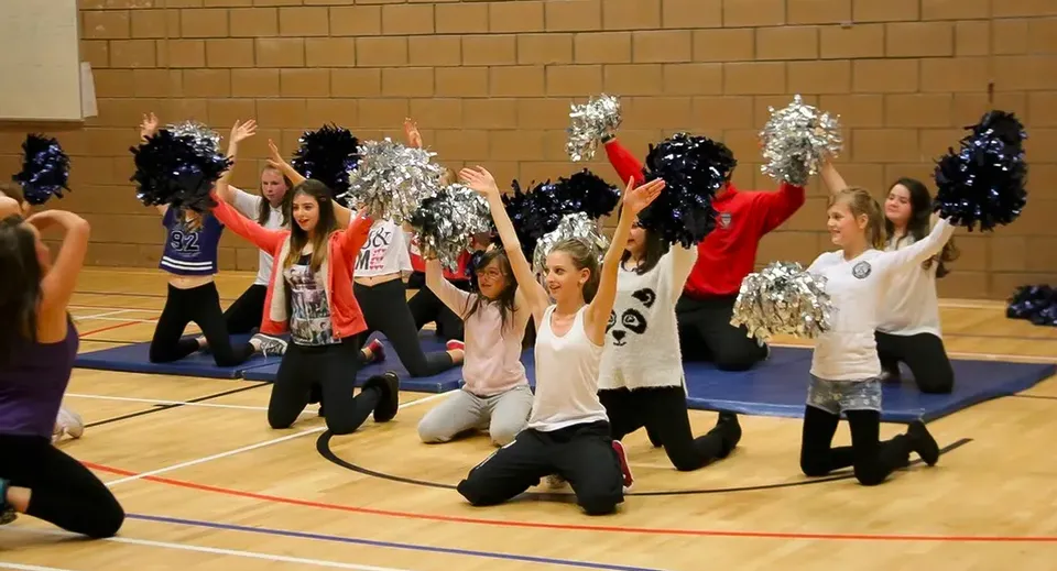 Un gruppo di cheerleader in divise colorate e con pompon si esibisce sul campo da basket della Currie Community High School.