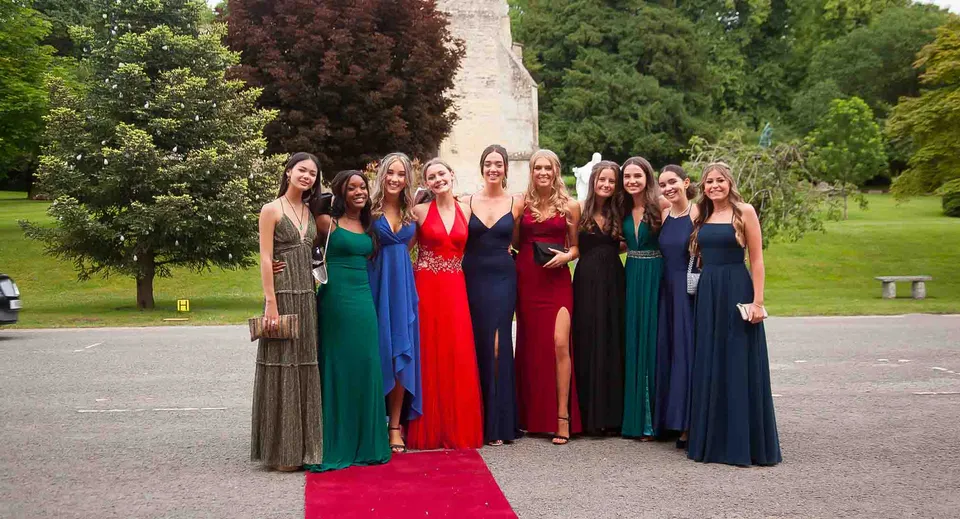 Un gruppo di giovani donne in abito da sera si trova insieme nel parco del campus del Thornton College.