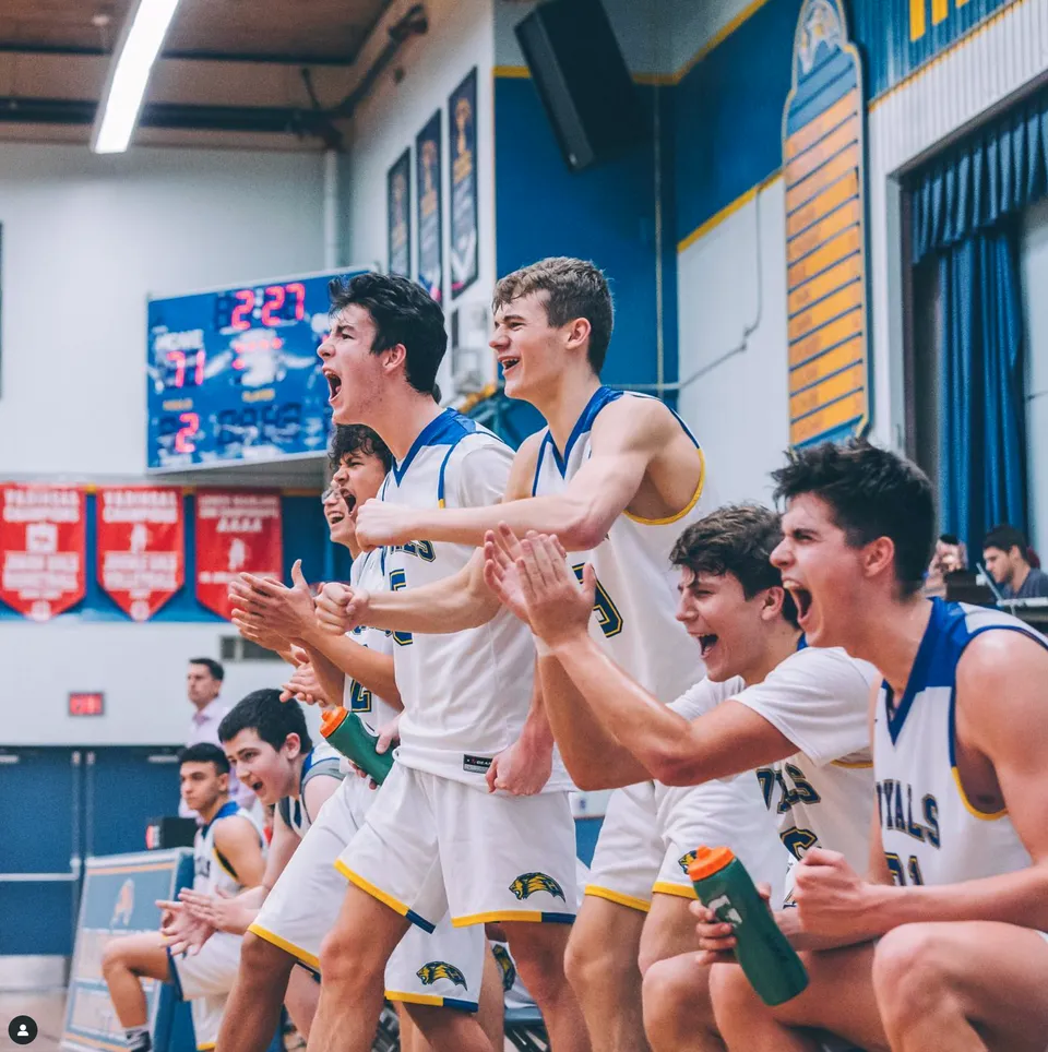 Un gruppo di giocatori di pallacanestro si trova sul campo e applaude all'interno del campus della Handsworth Secondary School.