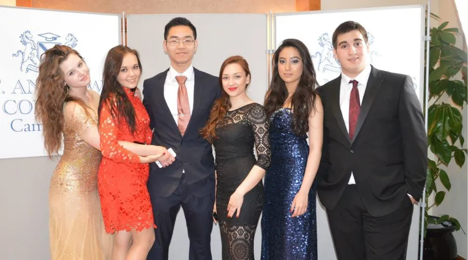 Sei persone posano a un evento nel campus del St. Andrew’s College Cambridge davanti a uno sfondo AMCHAM.