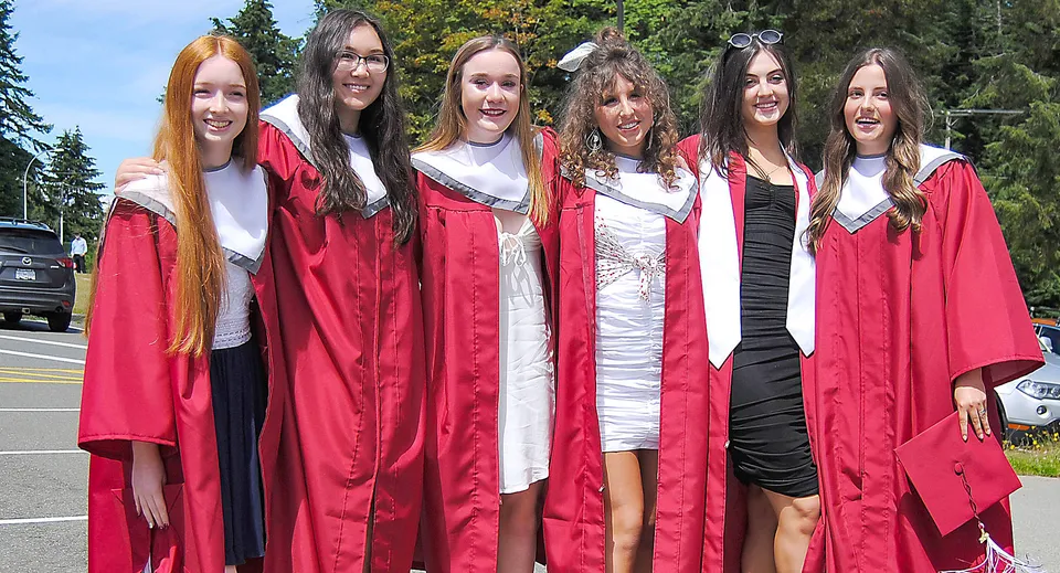Un gruppo di studentesse della Kwalikum Secondary School indossa toge rosse da diploma davanti a uno sfondo boscoso.