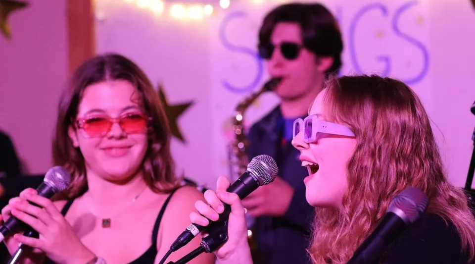 Tre persone della Proctor Academy si esibiscono con microfoni su un palco colorato.