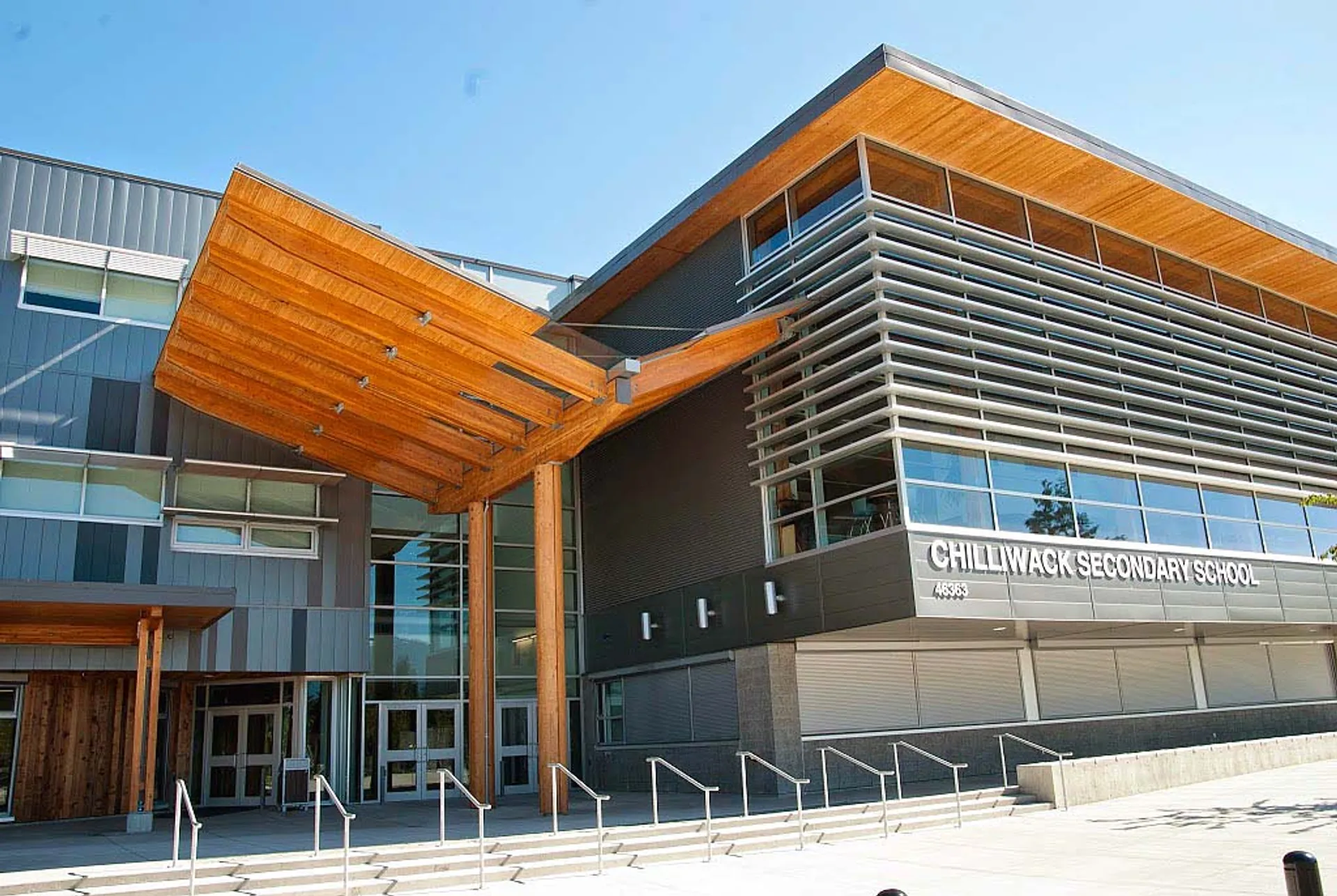 L'edificio moderno a più piani della Chilliwack Secondary School con facciata arancione e grigia e grandi vetrate sotto un cielo blu.
