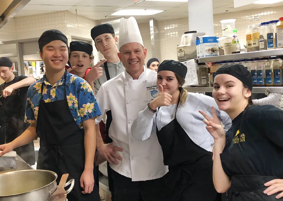 Studenti della Dover Bay Secondary School si radunano nella cucina della scuola insieme a uno chef in divisa bianca.