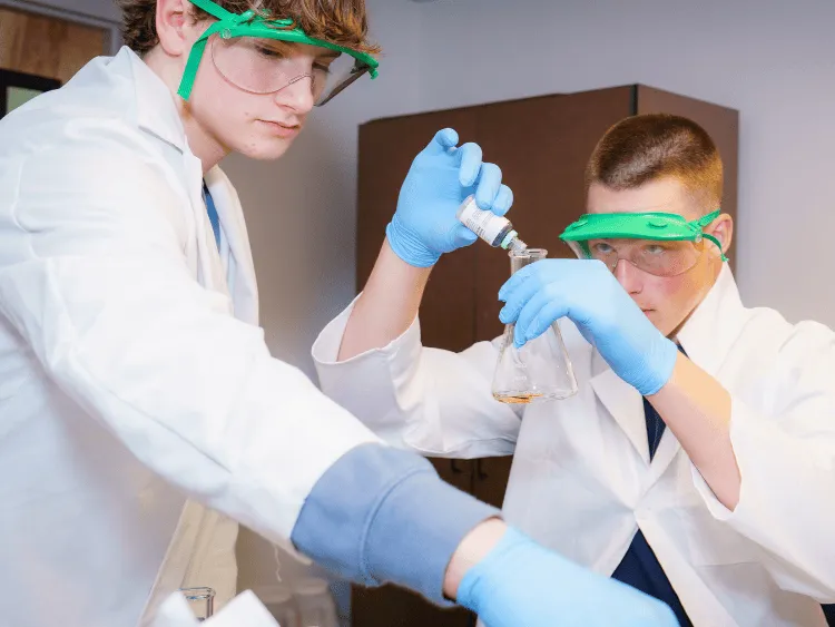 Dos alumnas con batas blancas de laboratorio realizan un experimento científico en el laboratorio de CATS Academy Boston.